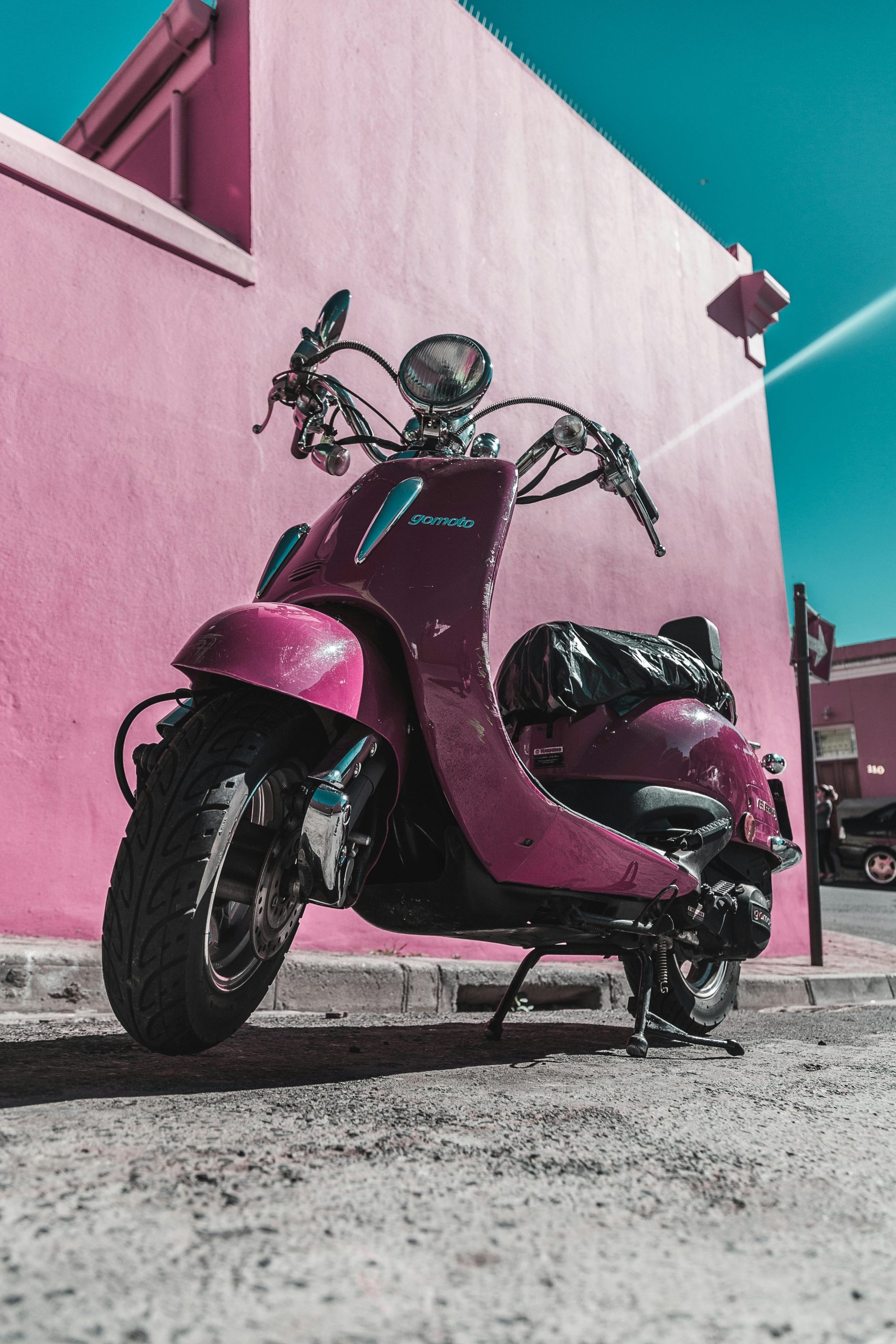 Home Vivid pink scooter parked against a colorful wall in Cape Town, South Africa.