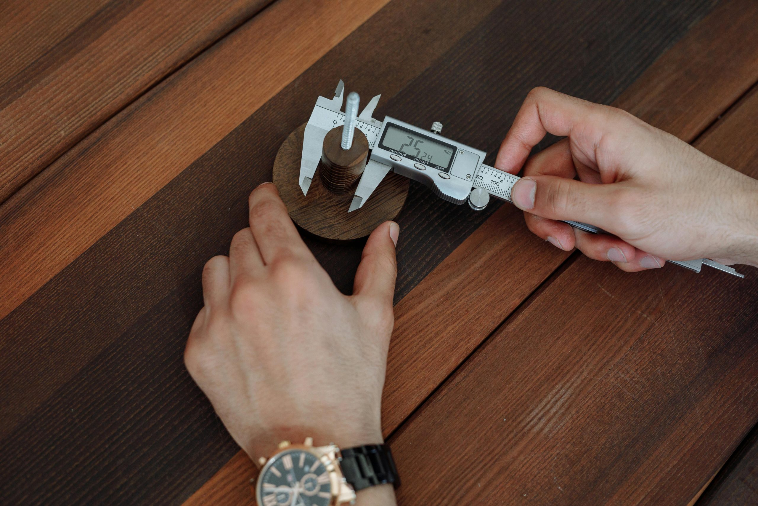 Detailed view of hands using a digital caliper on a wooden table.