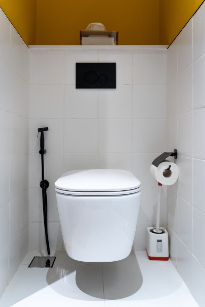 Clean and contemporary white bathroom with wall-mounted toilet, black flush panel, and bold yellow accents.
